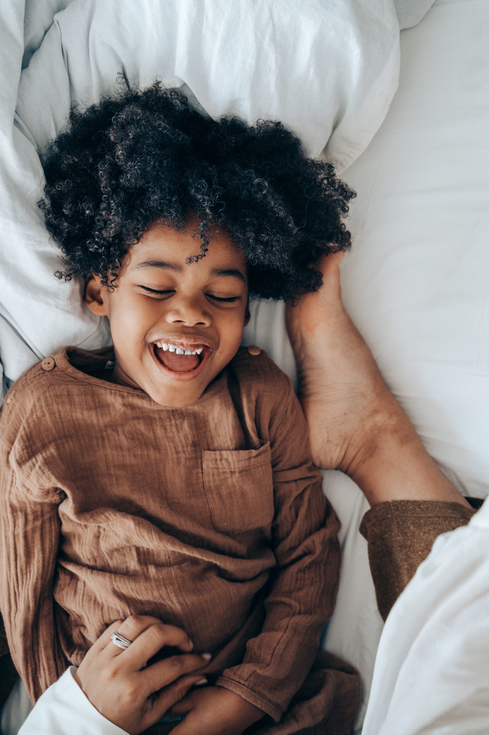 happy-african-american-boy-lying-on-bed-near-legs-of-mom-4545165