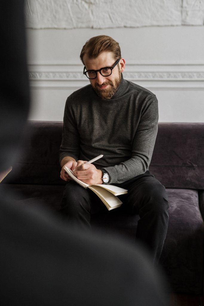 man-in-gray-sweater-and-black-pants-sitting-on-purple-couch-4100653