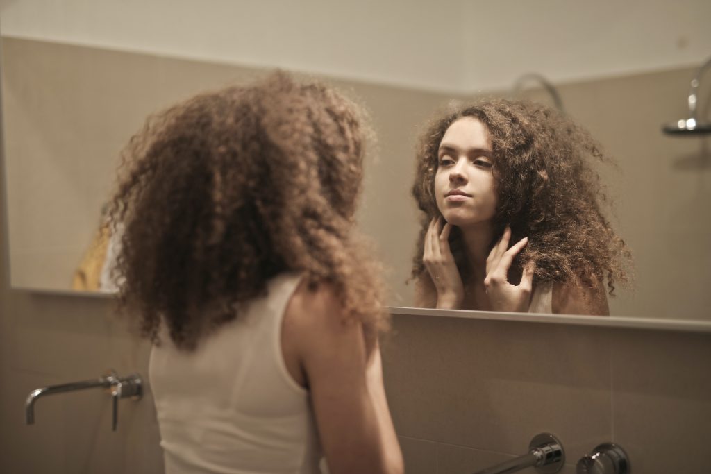 woman-in-white-tank-top-while-looking-herself-at-a-mirror-3811809